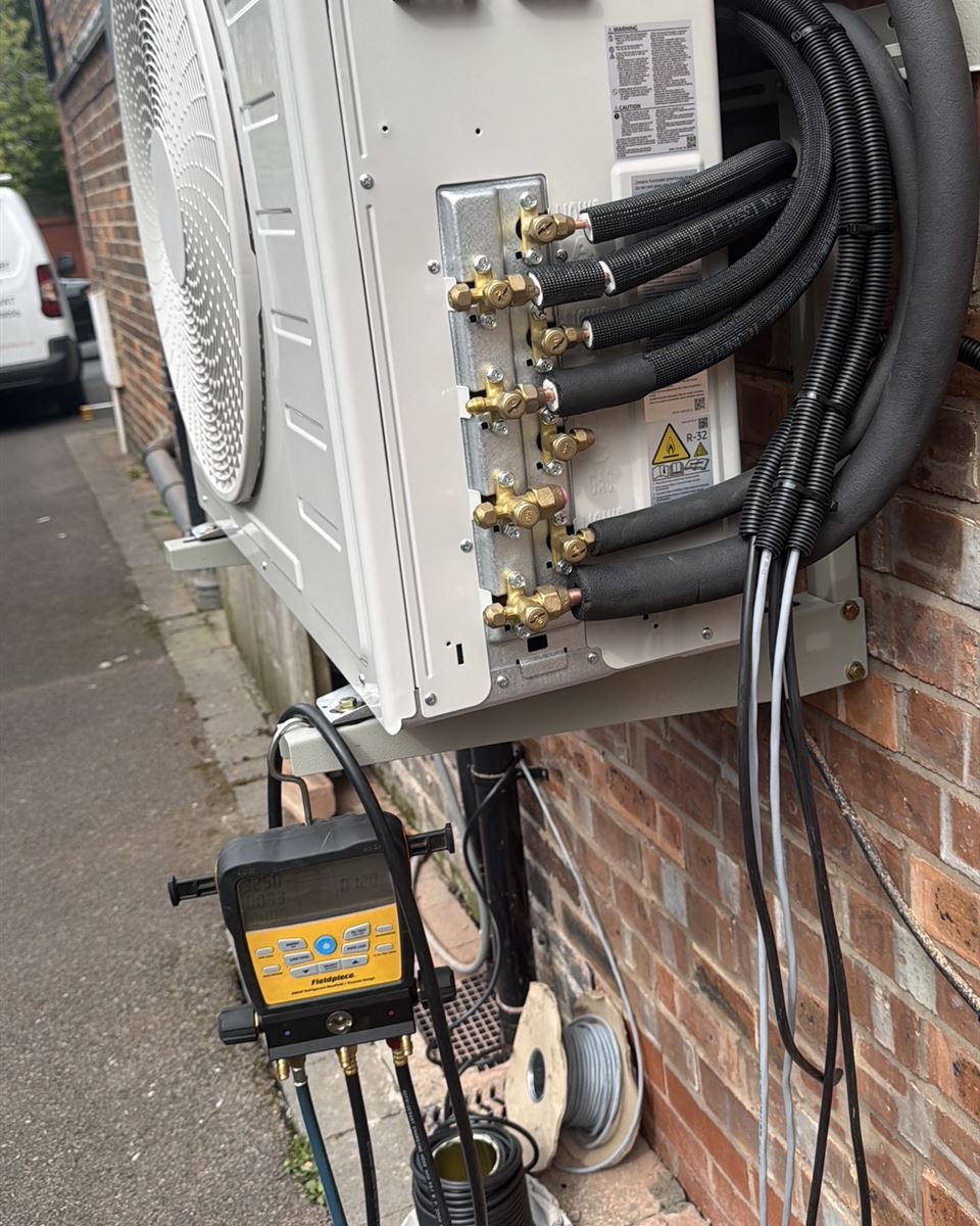 Samsung 8 kW multi-split outdoor unit on wall brackets during installation, with three insulated pipe pairs connected and a digital manifold attached