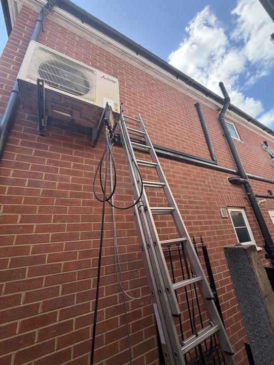 Engineer commissioning a Mitsubishi Electric outdoor unit with test gauges