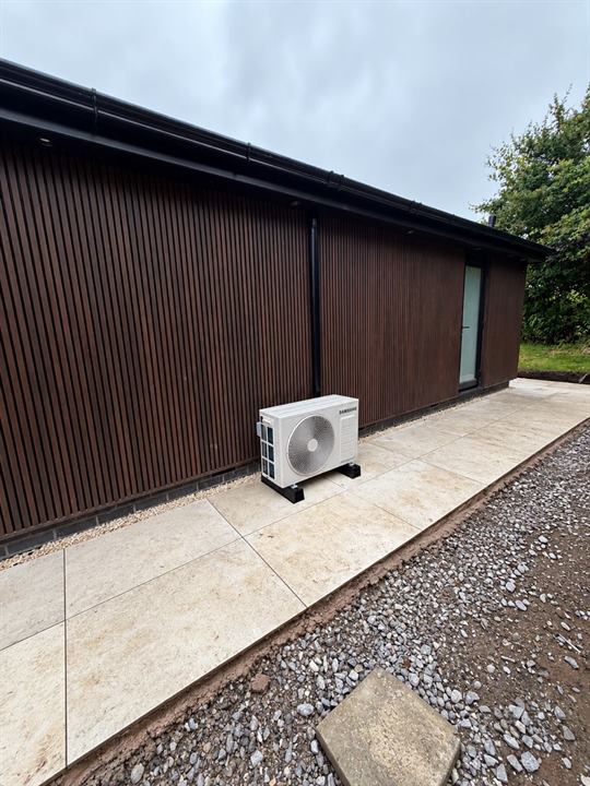 Samsung outdoor unit on anti-vibration feet on a patio beside a timber-clad summer house